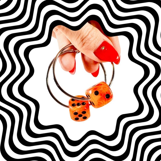 Hand holding a keychain with dice-shaped charms against a black and white wavy pattern