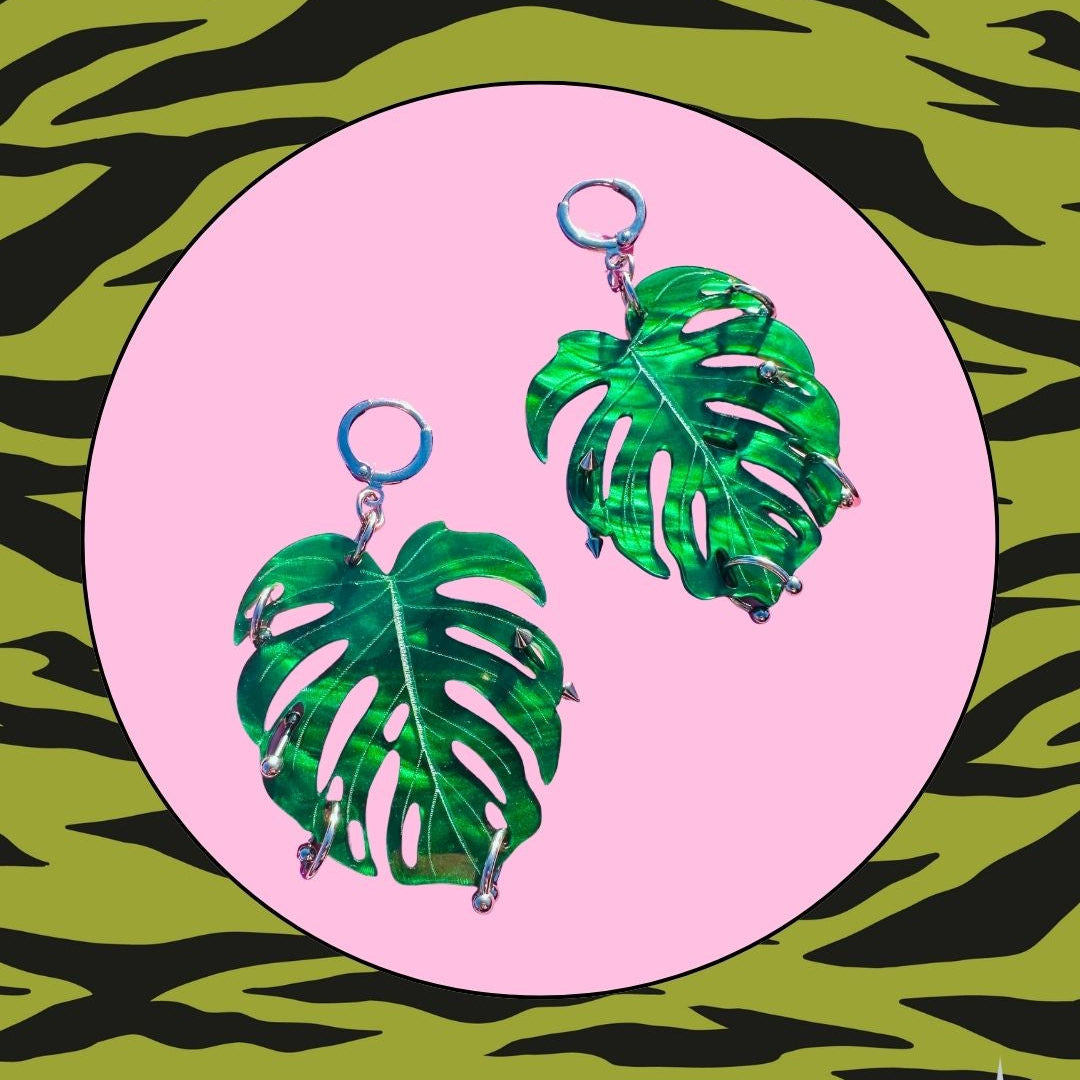Green leaf-shaped earrings on a pink circle with a green and black zebra print background