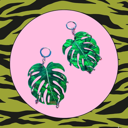Green leaf-shaped earrings on a pink circle with a green and black zebra print background
