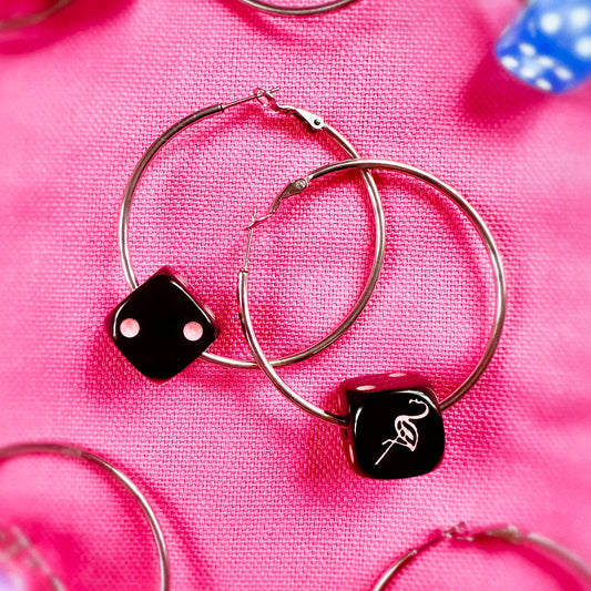 Hoop earrings with dice-shaped charms on a pink fabric background