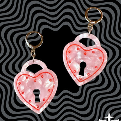 Heart-shaped lock keychains with pink glitter on a black and gray wavy background.