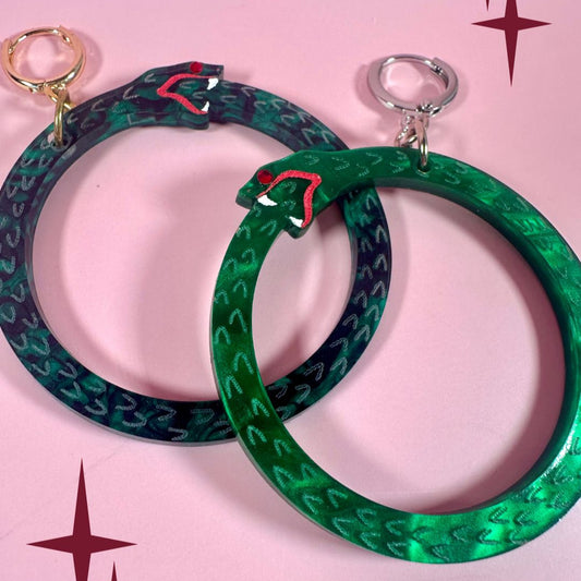 Two green hoop earrings with red accents on a pink background