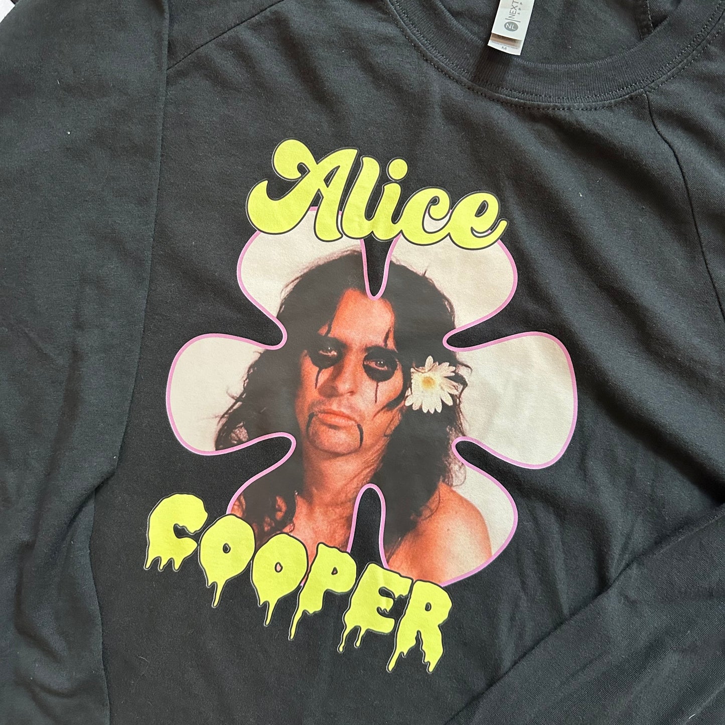A black long-sleeve graphic t-shirt featuring a portrait of Alice Cooper inside a pink and white flower outline, with 'Alice' in yellow at the top and 'COOPER' in yellow at the bottom.
