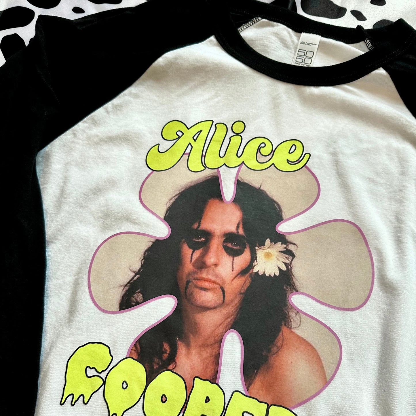 A black and white raglan t-shirt featuring a graphic of Alice Cooper inside a pink flower shape, with 'Alice' in yellow above and 'COOPER' in yellow below.