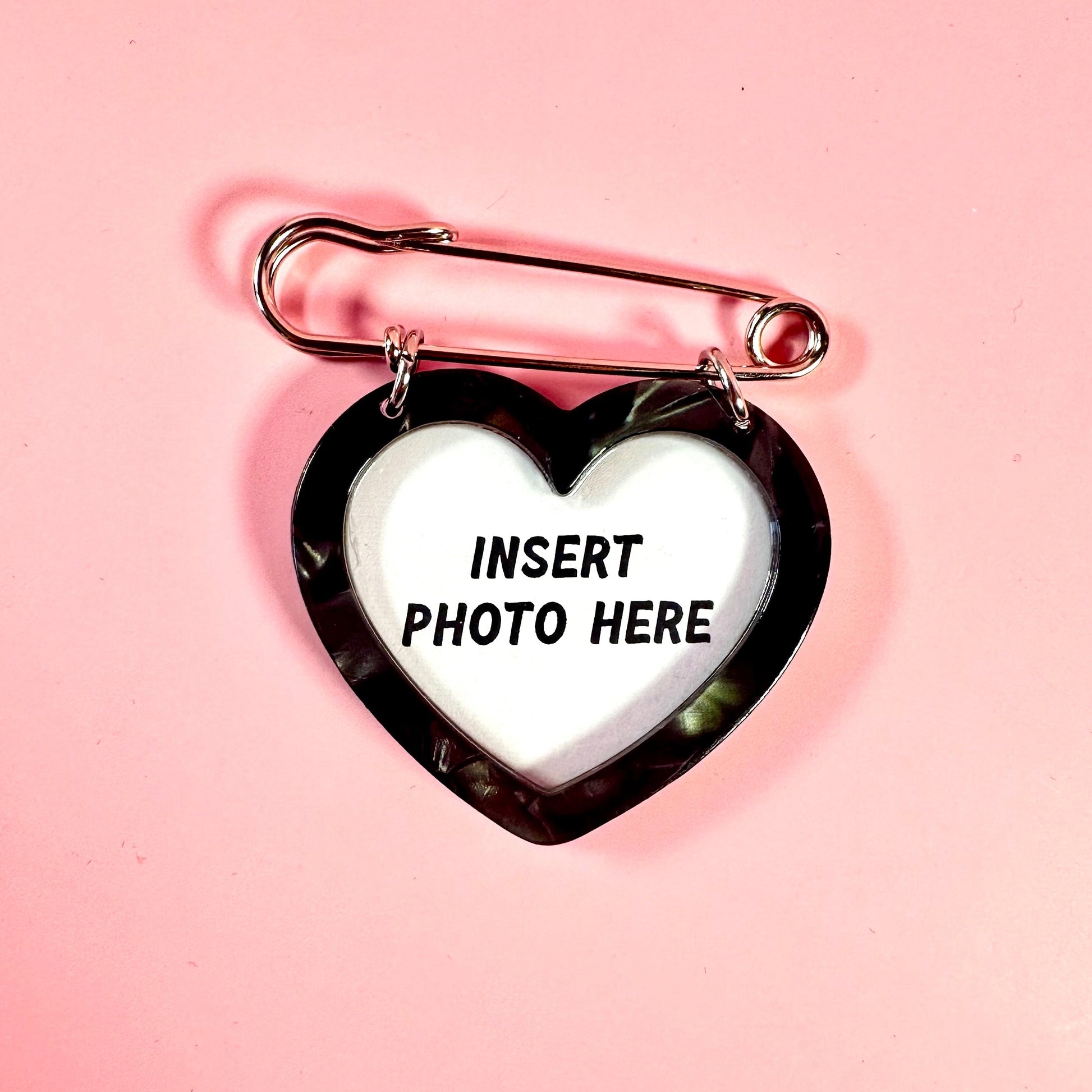 Heart-shaped photo frame with a safety pin on a pink background
