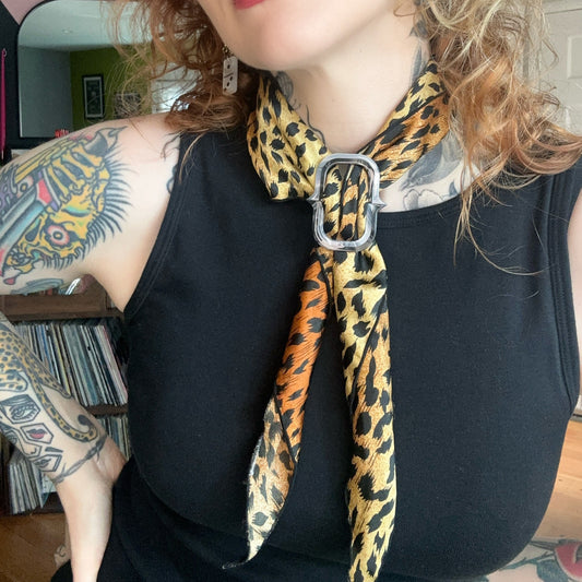 chainlink scarf ring in grey colors on a leopard print neck scarf on a woman in a black tank dress with red and blonde hair and tattoos
