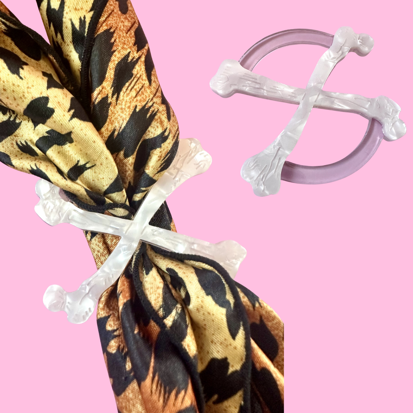 A leopard-print scarf tied with a clear cross-shaped bone ring, shown alongside a matching clear cross-shaped bone ring on a solid pink background.