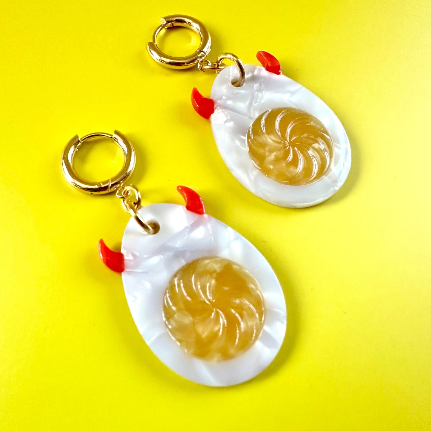 A pair of novelty earrings shaped like stylized white chickens with gold-tone rings and small red comb accents, displayed on a bright yellow background.