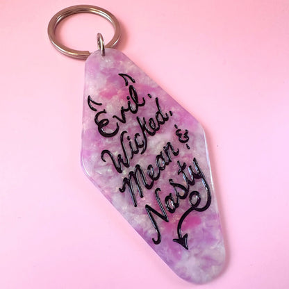 A hotel keychain shaped like a tilted coffin, featuring a marbled pink and purple resin body with the text 'Evil. Wicked.
