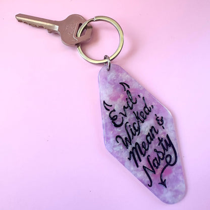 A keychain with a purple and pink marbled charm featuring the text 'Evil, Wicked, Mean & Naughty' in black script, attached to a silver metal keyring with a key on a solid light pink background.