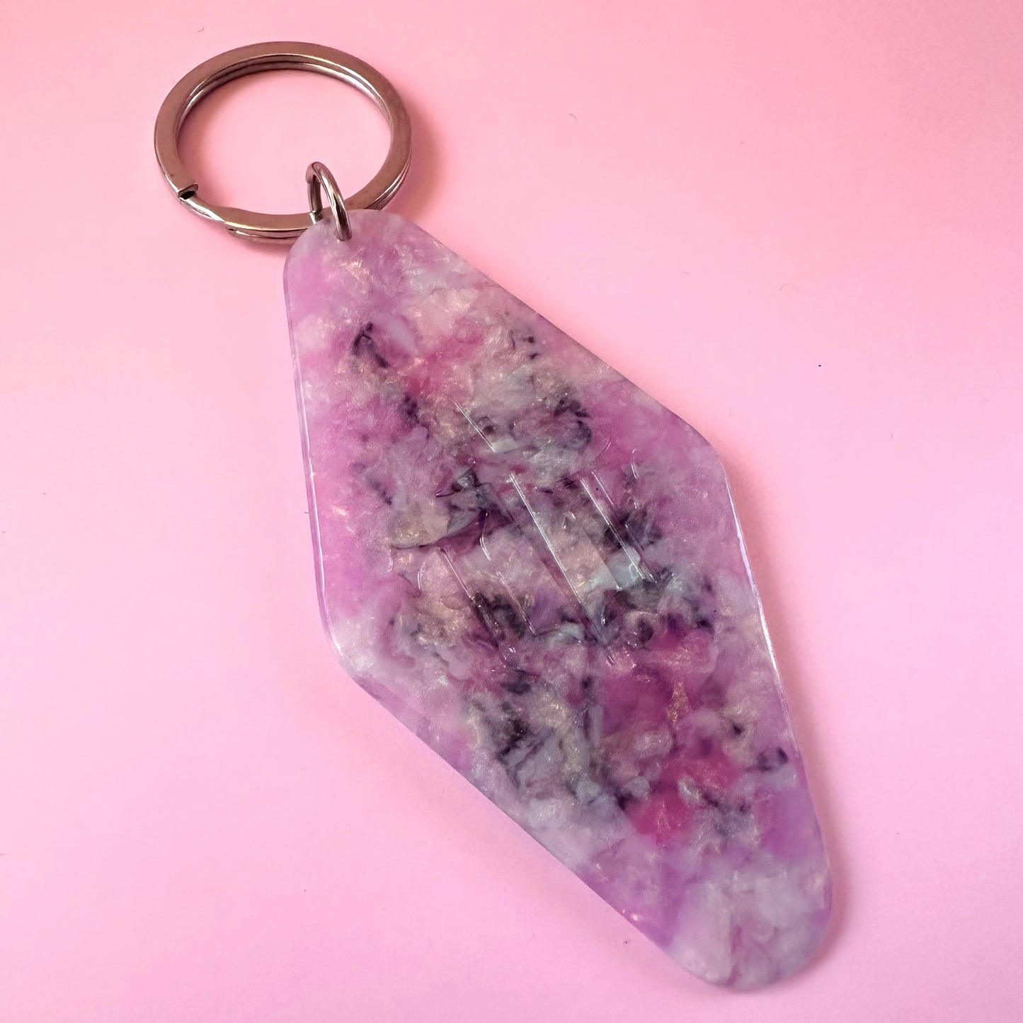 A pink and purple marbled crystal keychain with a silver metal split ring, shown on a solid pink background.