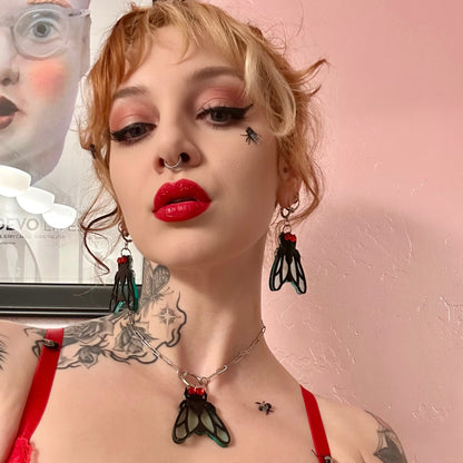 Person with tattoos and red lipstick wearing a black and red outfit against a pink background