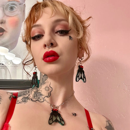 Person with tattoos and red lipstick wearing a black and red outfit against a pink background