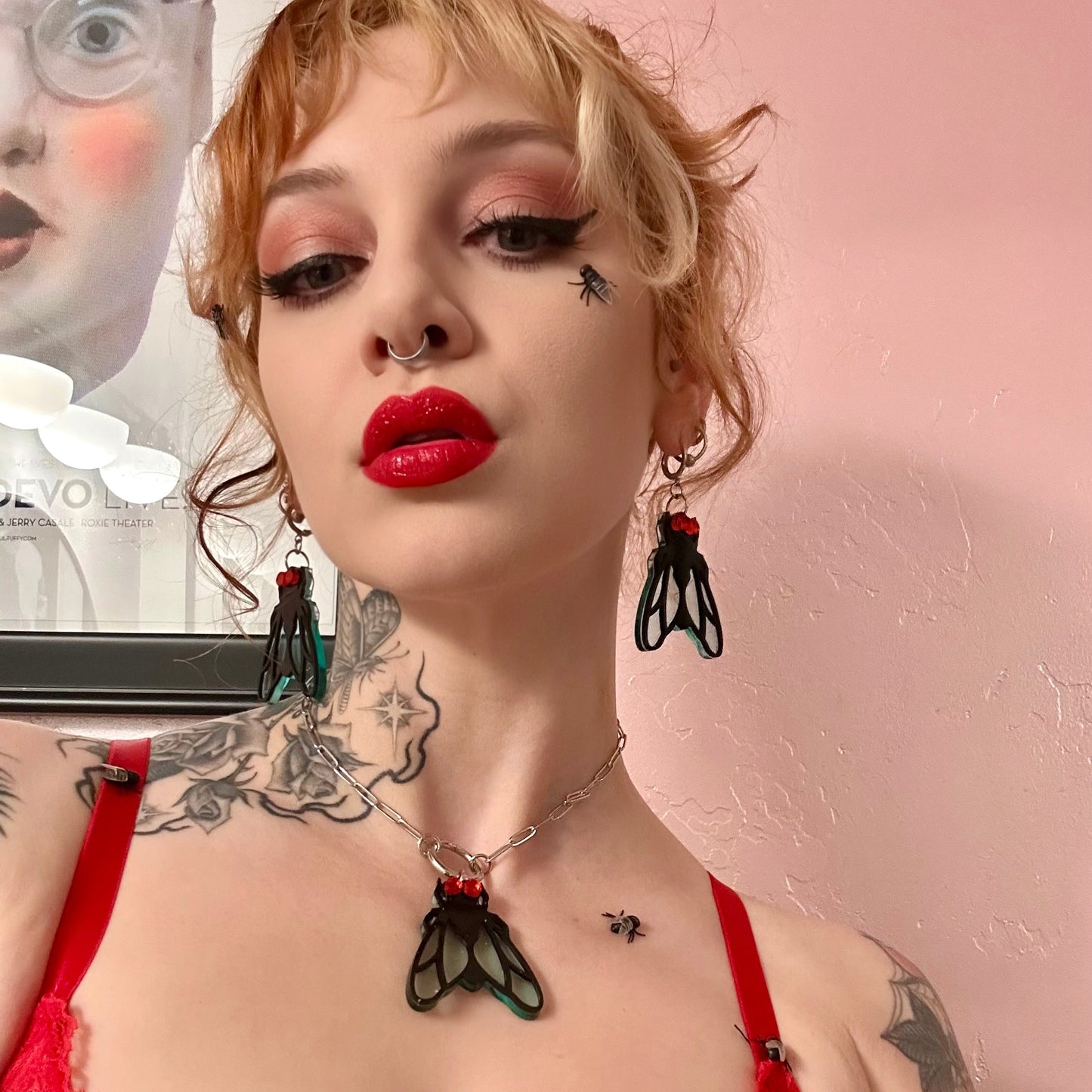 Person with tattoos and red lipstick wearing a black and red outfit against a pink background