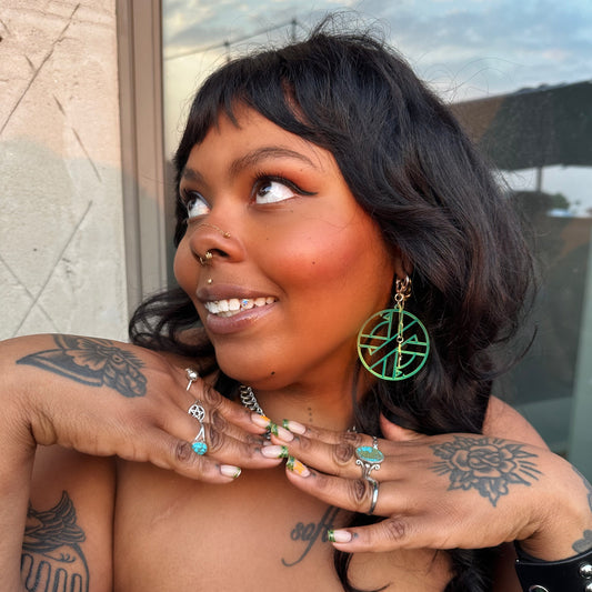 Woman with tattoos and earrings leaning against a wall.