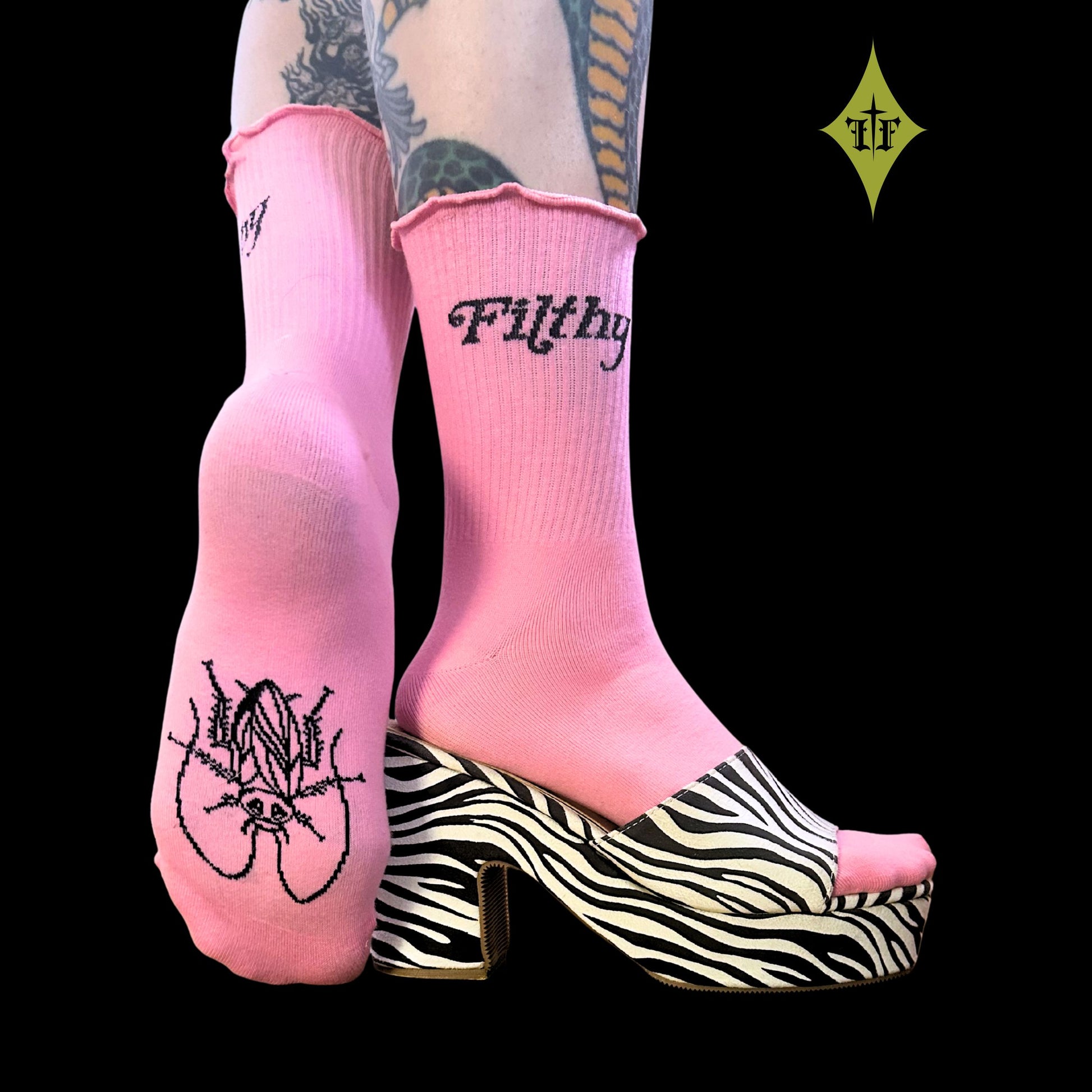 Pink crew socks with black gothic text and graphic designs, worn with a zebra-print platform mule on a solid black background.