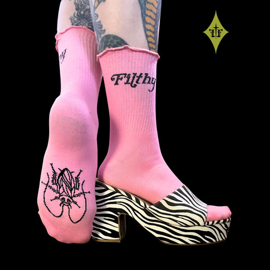Pink crew socks with black gothic text and graphic designs, worn with a zebra-print platform mule on a solid black background.