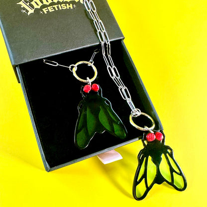A novelty keychain necklace featuring a green fly pendant with red eyes, shown next to its black presentation box on a bright yellow background.