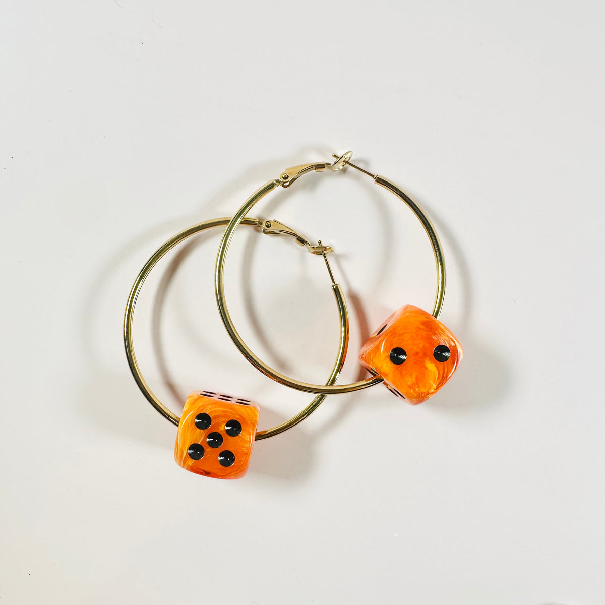 Gold hoop earrings with orange dice-shaped charms on a white background