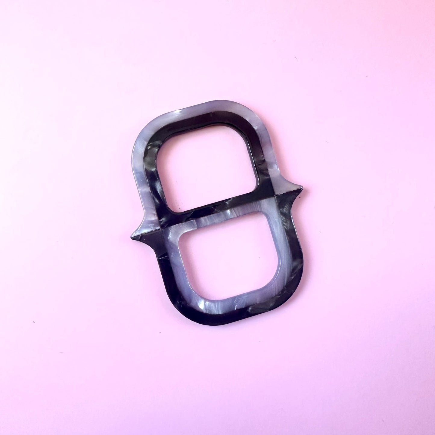 A single black and gray marbled ring-shaped scarf ring with a glossy finish, photographed on a solid light pink background.
