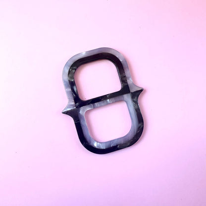 A single black and gray marbled ring-shaped scarf ring with a glossy finish, photographed on a solid light pink background.