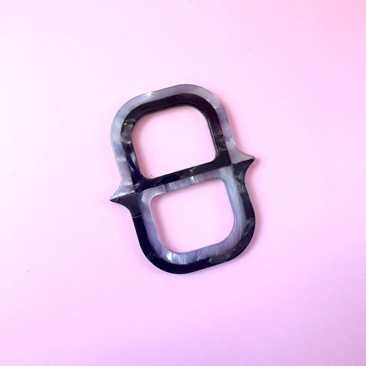 A single black and gray marbled ring-shaped scarf ring with a glossy finish, photographed on a solid light pink background.