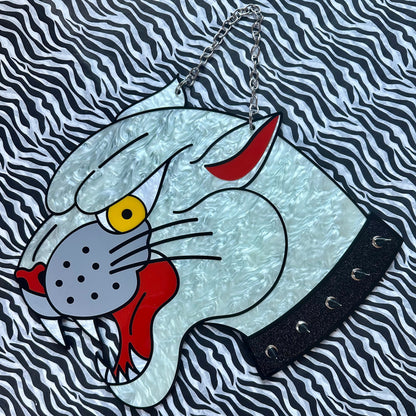 A handbag featuring a stylized panther head patch in light blue, red, yellow, and gray, with a black studded collar detail and a silver chain strap, set against a black and white zebra-print fabric background.