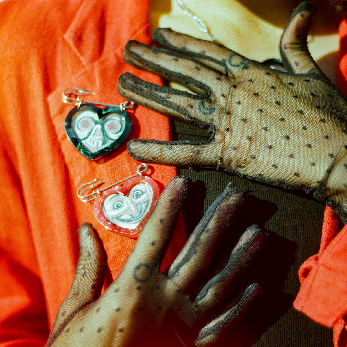 Black and red heart shaped picture frame safety pins on a red coat on a woman wearing a black tank top and black sheer gloves