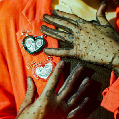 Black and red heart shaped picture frame safety pins on a red coat on a woman wearing a black tank top and black sheer gloves
