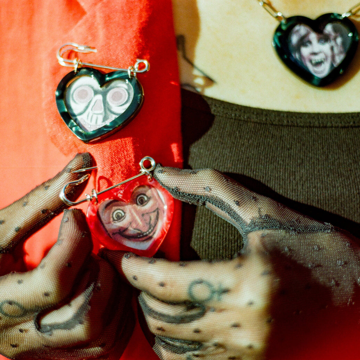 Black and red heart shaped picture frame safety pins on a red coat on a woman wearing a black tank top and black sheer gloves