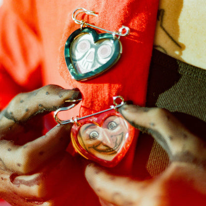 Black and red heart shaped picture frame safety pins on a red coat on a woman wearing a black tank top and black sheer gloves