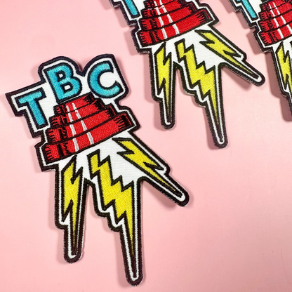 Three 'TBC' logo patches with lightning bolts on a pink background