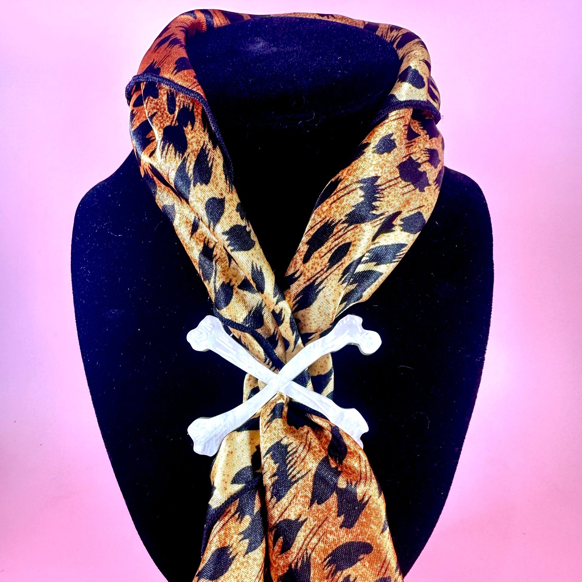 Leopard print scarf with bone-shaped clips on a black mannequin against a pink background