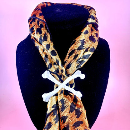Leopard print scarf with bone-shaped clips on a black mannequin against a pink background