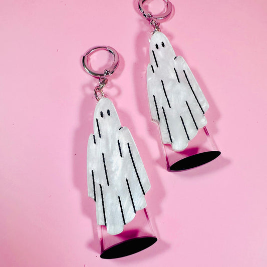 Two ghost-shaped earrings on a pink background