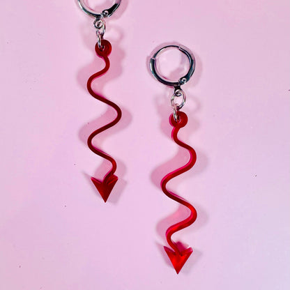 Red arrow-shaped earrings on a pink background