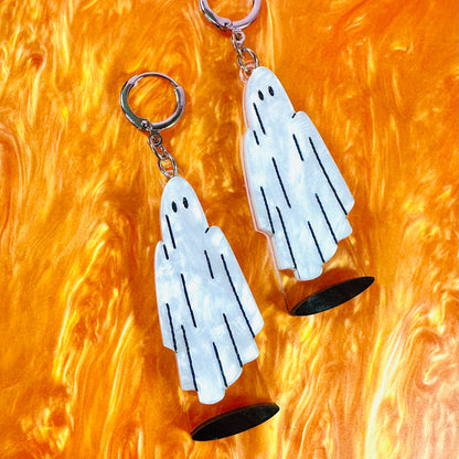 Ghost-shaped earrings on a textured orange background