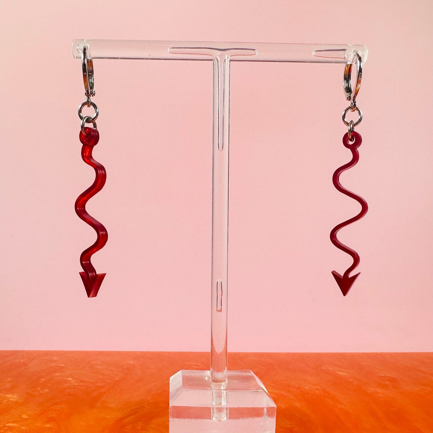 Red spiral earrings on a clear stand with a pink and orange gradient background