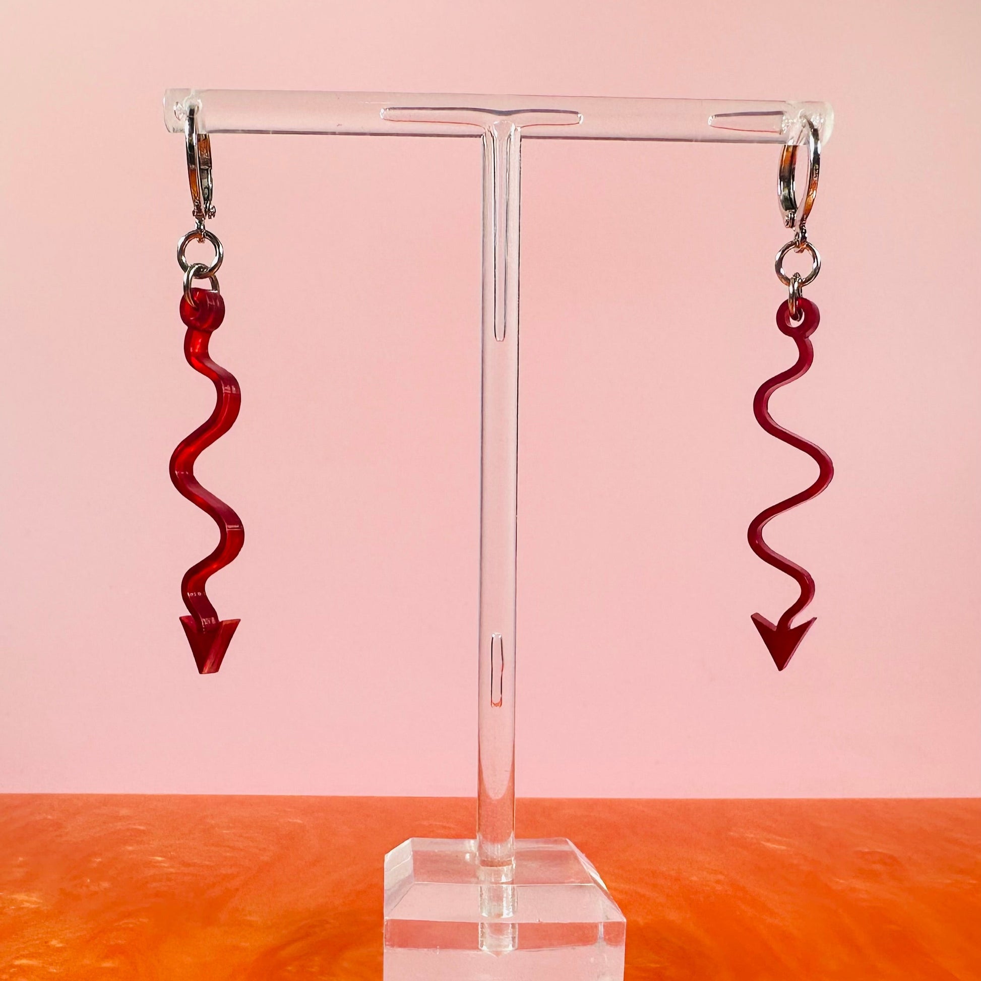 Red spiral earrings on a clear stand with a pink and orange gradient background