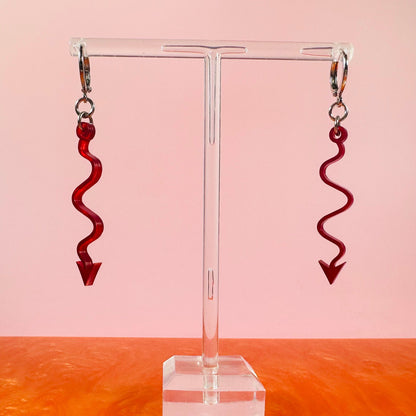 Red spiral earrings on a clear stand with a pink and orange gradient background