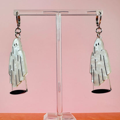 Pair of ghost-shaped earrings on a clear stand with a pink background