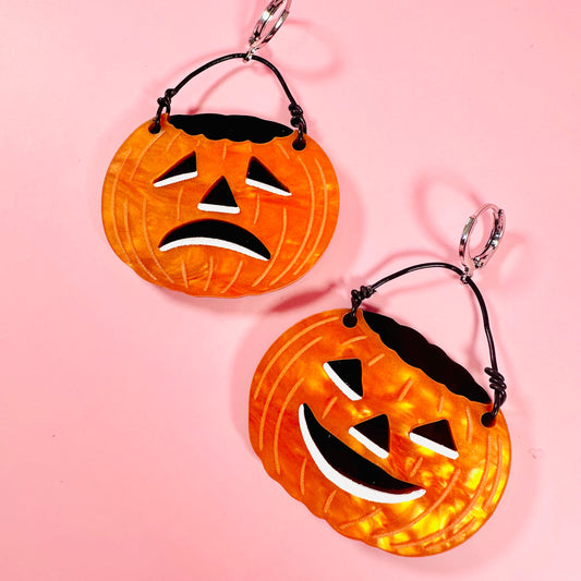 Halloween-themed earrings with jack-o'-lantern design on a pink background