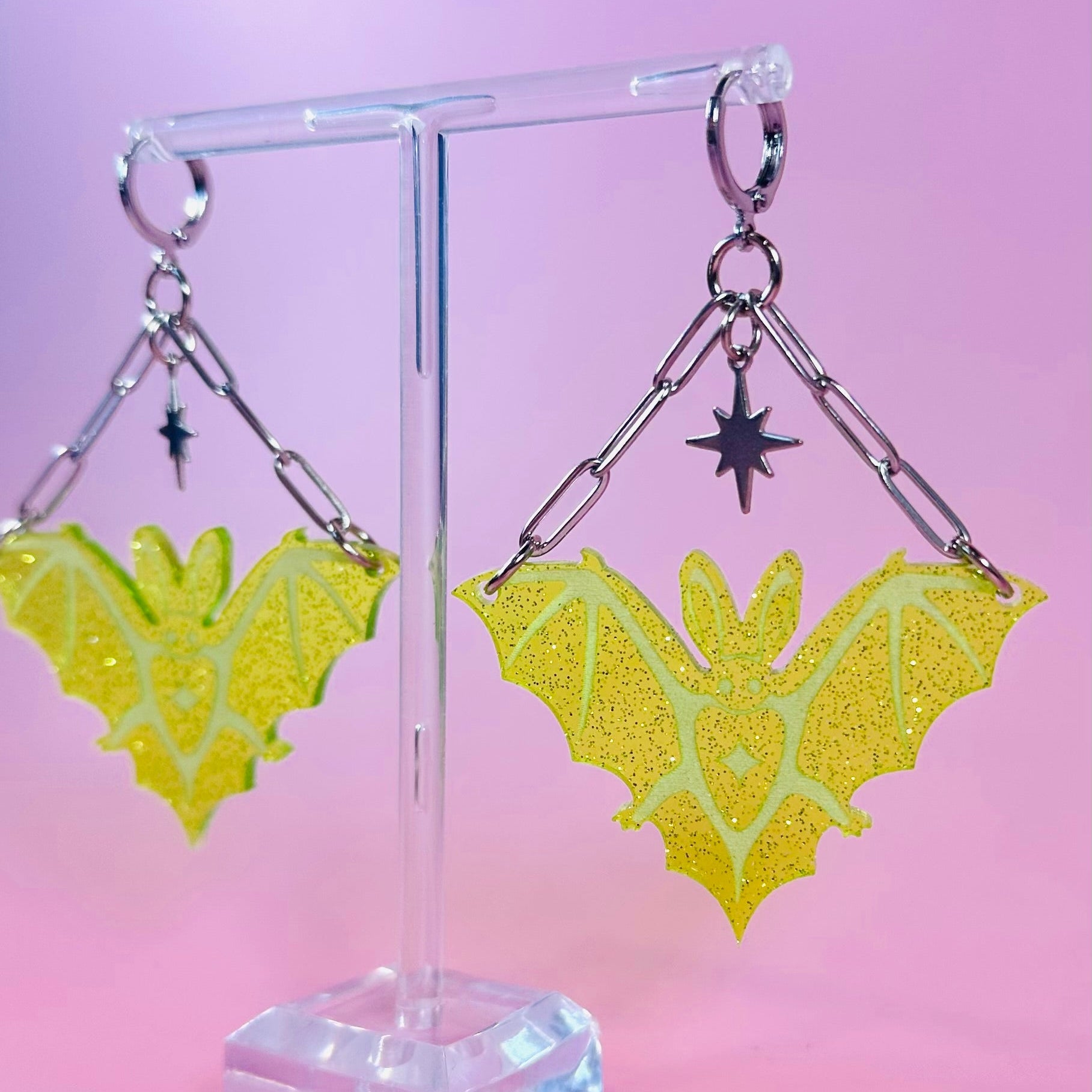 Yellow butterfly-shaped earrings on a clear stand against a pink background