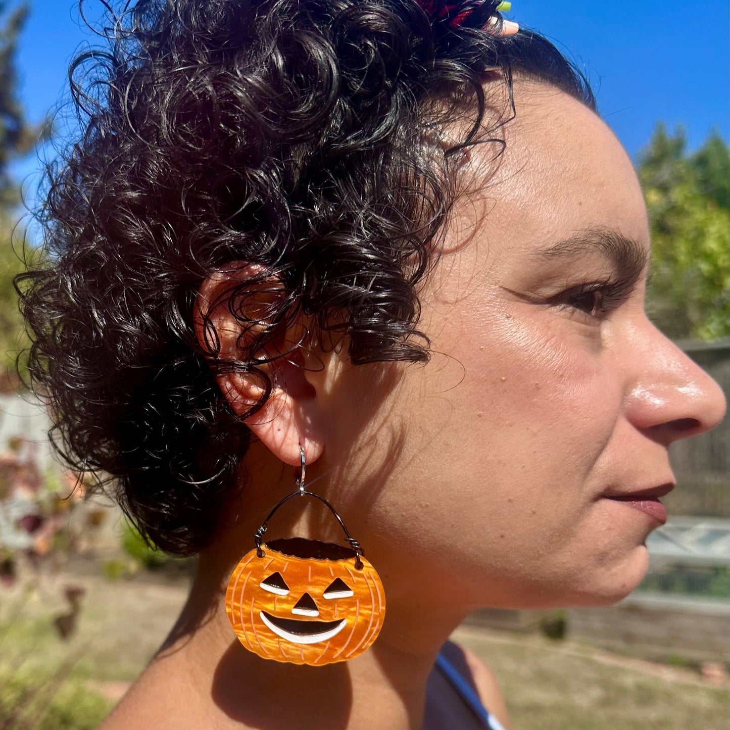 Person wearing Halloween-themed earrings with a pumpkin design outdoors.