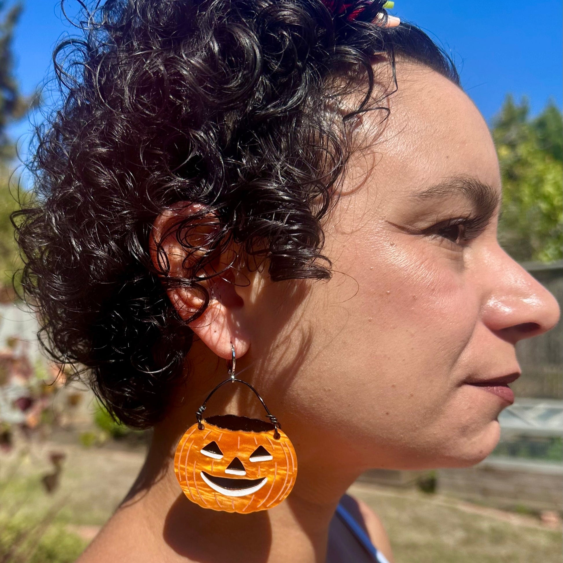 Person wearing Halloween-themed earrings with a pumpkin design outdoors.