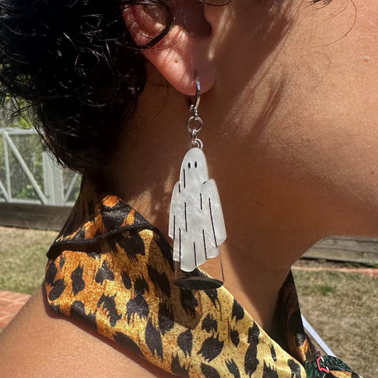 Person wearing a leopard print sleeve with ghost-shaped earrings.