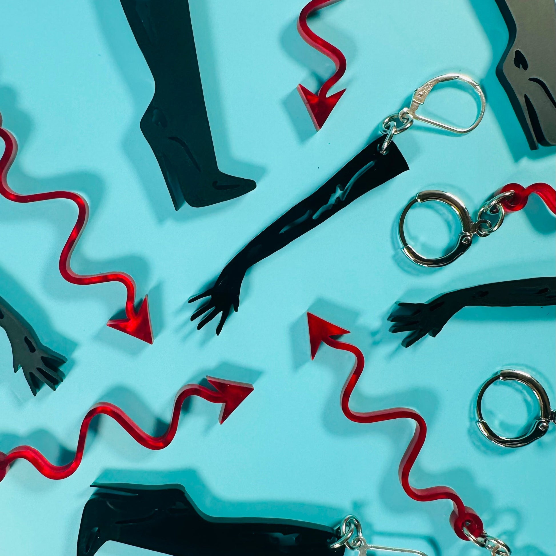 Earrings with black boots, red whips, and silver handcuffs on a light blue background