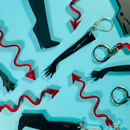 Earrings with black boots, red whips, and silver handcuffs on a light blue background