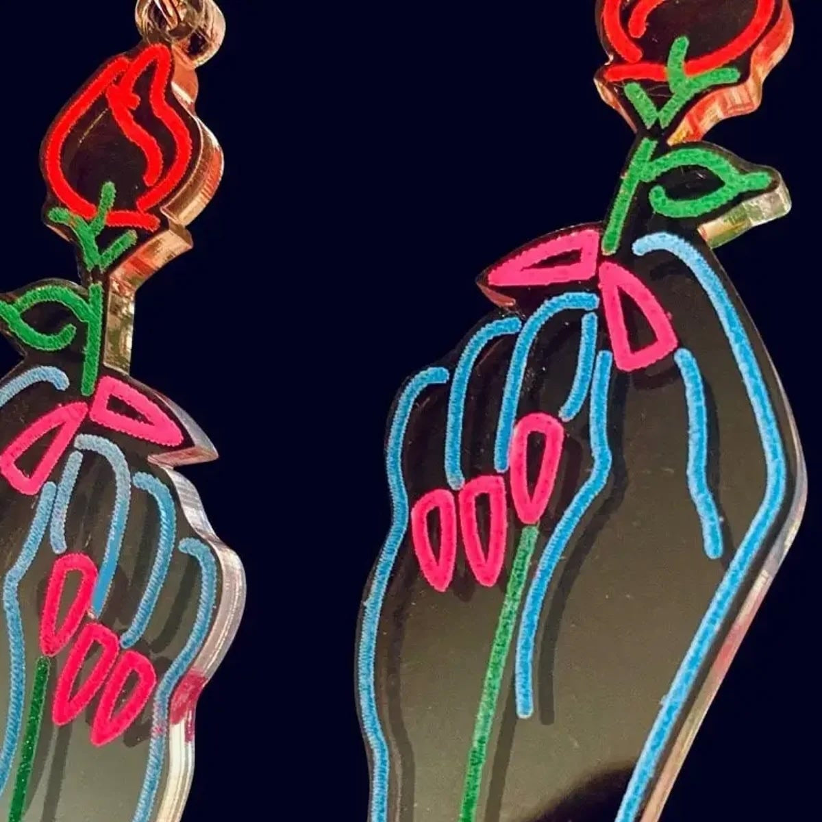 Neon-style hand and flower earrings on a black background