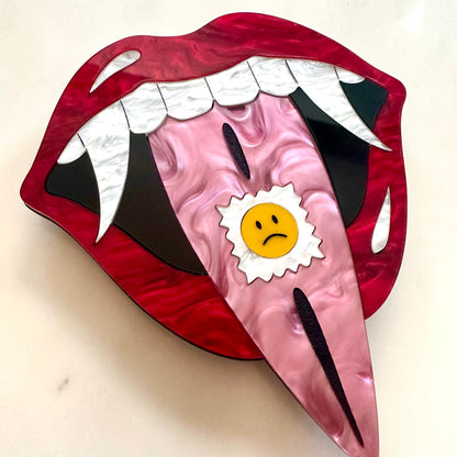Cartoonish mouth design with a sad face sticker on a beige background